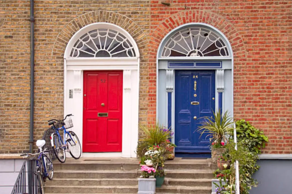 Two adjacent doors, one painted in vibrant red and the other in dark blue. A bicycle and assorted plants add to the colorful allure.