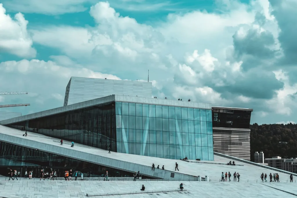 An architectural glimpse of Oslo's Opera House, where people are seen wandering around.
