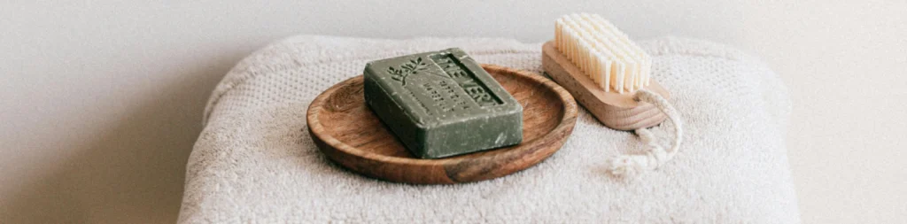On top of the pristine white towels lie a bar of verdant green soap and a wooden brush.